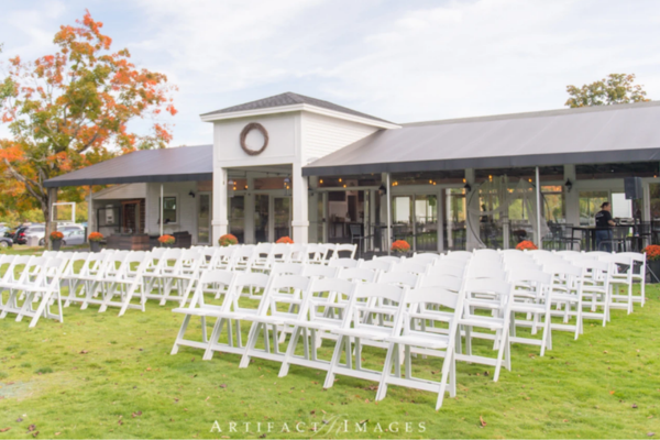 A view of the reception lawn at The Farmhouse with white chairs and orange, fall florals