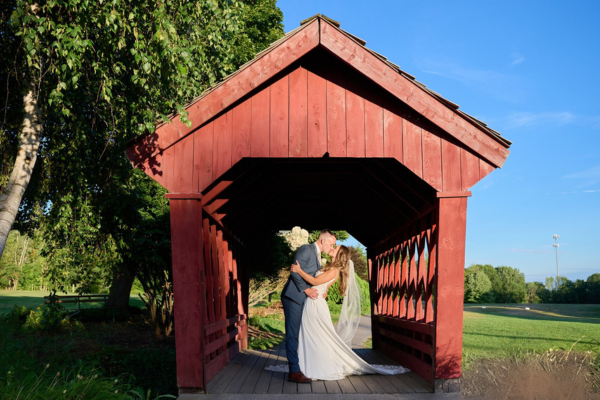 Couple posing in the red barn area with lush greenery surrounds
