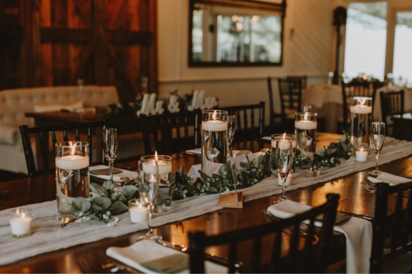 Table setting in the reception room at The Farmhouse, with wood elements and floating candles with greenery and white linens